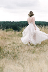 Fototapeta na wymiar Bride running in dress through a field