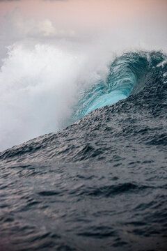 A beautiful blue wave of water turns for a surfer to surf it in Tahiti 