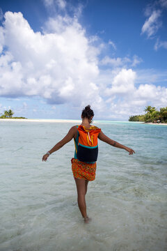 A woman walks into the water in an orange dress and backpack in Tahiti 