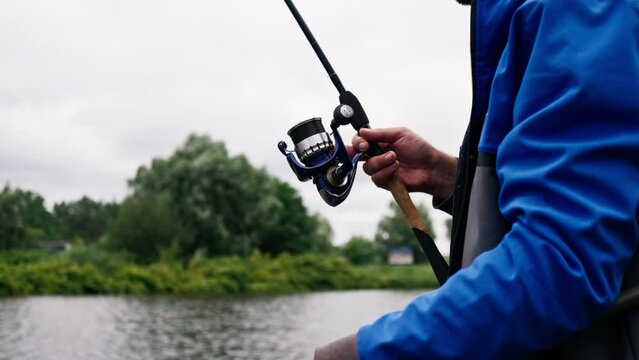 Fisherman with fishing rod or spinning and professional tools sitting on the river bank rear view Pull fish out of the lake sports fishing