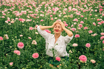 Young beautiful pretty girl sitting on bushes of roses in blossom