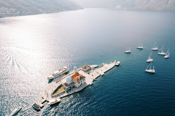 Motor boats and sailboats are moored around the island of Gospa od Skrpjela. Montenegro. Drone - obrazy, fototapety, plakaty