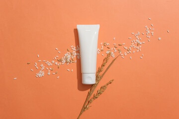 An unlabeled white tube is placed in the center of the frame with white rice on an orange background. Vegan cosmetics concept with rice extract. Copy space.