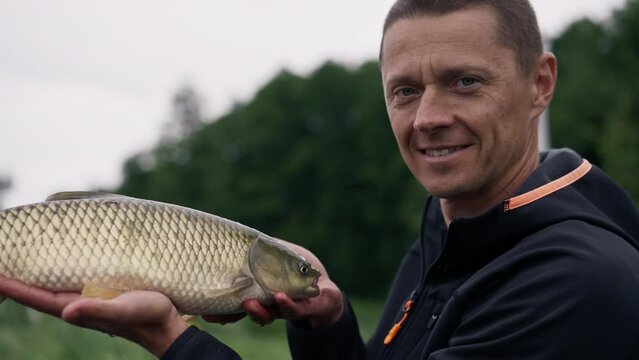 portrait of a professional fisherman holding a carp fish on the bank of a river fishing in reservoirs a good catch