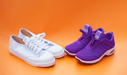 Two pairs of white and purple canvas sneakers. Orange background. Comfortable, fashionable. Concept, shoes for doing sport or exercise also can wear for traveling, hiking.   