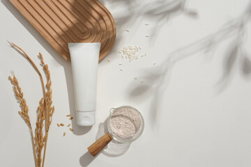 Wooden-handled glass bowl filled with rice bran powder. Unbranded facial cleanser tube, rice, and a domed podium on a white backdrop with soft shadows. A captivating setup for advertising.
