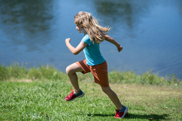 Kid boy running on green grass near lake in summer park. Child running outdoor. Healthy sport...