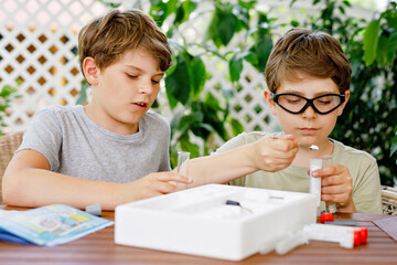 Two kids boys doing chemical experiment in laboratory at school. Children with protective glasses study using pipette dropping liquid to test tube , caucasian , biochemistry . chemistry class.