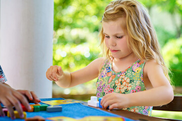 Little preschool girl playing board game with colorful bricks. Happy child build tower of wooden...