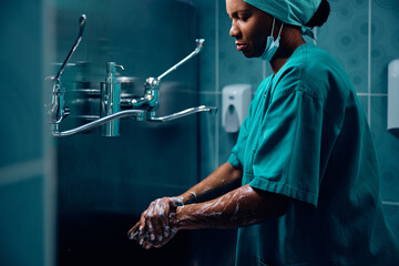 Black female doctor washing hands before surgery in hospital.