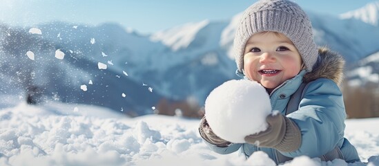 Joyful toddler playing in the snowy mountains, making a snowball.