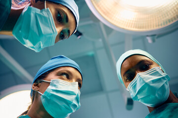 Below view of female surgeons above patient in operating room. - obrazy, fototapety, plakaty