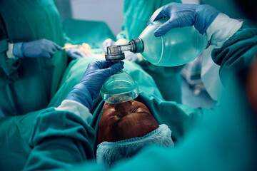 Close up of anesthesiologist using oxygen mask on patient during surgery in hospital.