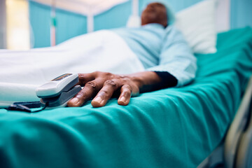 Close up of black patient with pulse oximeter on his finger recovering after surgery.