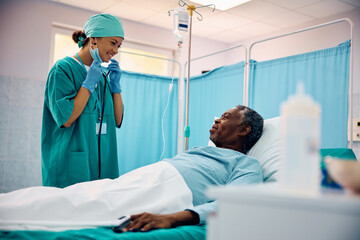 Happy female surgeon visiting African American senior patient who is recovering at intensive care unit.