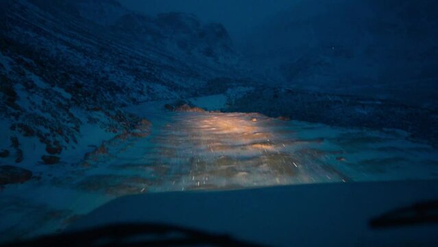 POV shot of vehicle driving on snowy road in Himalayas during snowfall at Manali, India. Slippery road during winters. Risky road in the mountains. Snowfall during night.