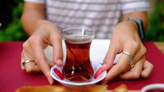 woman enjoys traditional Turkish breakfast on garden. She sits at table surrounded by greenery. woman stirring sugar in tea in a traditional Turkish tea cup called bardak