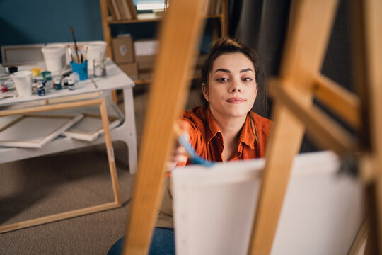 Young woman painter sitting in front of the canvas and drawing. Working in artist studio. Creative concept
