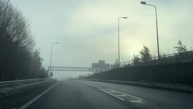Car windscreen view driving up the slip road, joining Manchester ring road M60 motorway traffic at junction J10 in winter fog, England, UK.