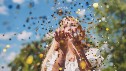 The girl blows a golden confetti out of her hands.