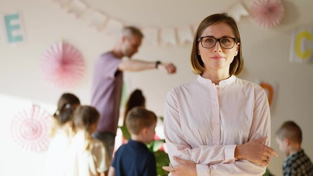 Portrait of a teacher girl with glasses and a pink shirt who smiles with her arms crossed on her chest against the background of a biology lesson for preschool children together with a male teacher in
