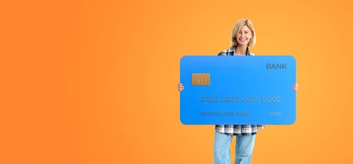 Foto op Canvas Smiling woman standing with credit card on empty orange background © ImageFlow