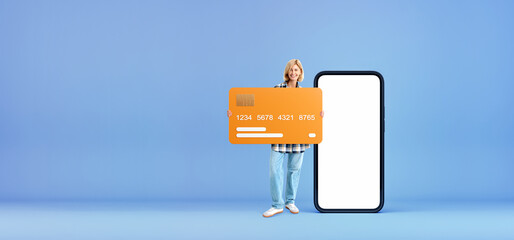 Cheerful woman with big credit card and blank smartphone screen