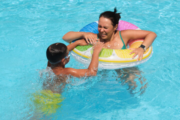A boy grips a colorful float as his mother smiles; a sunny pool scene. This image ties to the joy of active parenting.