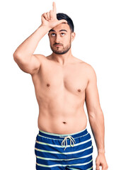Fototapeta premium Young handsome man wearing swimwear making fun of people with fingers on forehead doing loser gesture mocking and insulting.