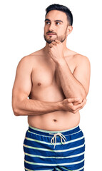 Fototapeta premium Young handsome man wearing swimwear with hand on chin thinking about question, pensive expression. smiling and thoughtful face. doubt concept.