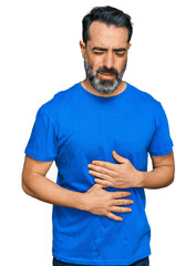 Middle aged man with beard wearing casual blue t shirt with hand on stomach because indigestion, painful illness feeling unwell. ache concept.