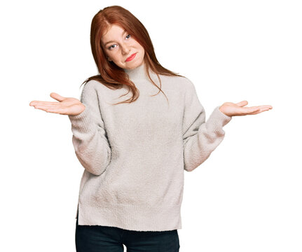 Young read head woman wearing casual winter sweater clueless and confused expression with arms and hands raised. doubt concept.