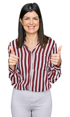 Beautiful brunette woman wearing striped shirt success sign doing positive gesture with hand, thumbs up smiling and happy. cheerful expression and winner gesture.