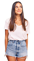 Obraz premium Young hispanic woman wearing casual white tshirt smiling looking to the side and staring away thinking.
