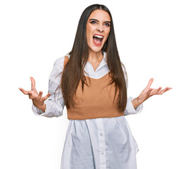 Young beautiful woman wearing casual white shirt crazy and mad shouting and yelling with aggressive...