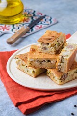 Sliced savory pie with canned tuna, boiled egg and green onions on a ceramic plate on a gray concrete background.