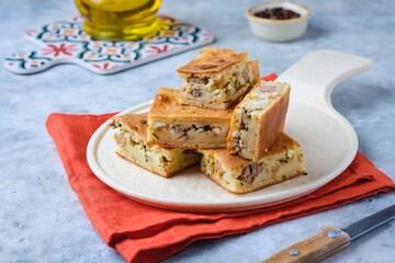 Sliced savory pie with canned tuna, boiled egg and green onions on a ceramic plate on a gray concrete background.