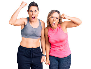 Couple of women wearing sportswear angry and mad raising fist frustrated and furious while shouting with anger. rage and aggressive concept.