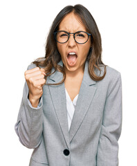 Young brunette woman wearing business clothes angry and mad raising fist frustrated and furious...