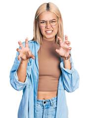 Obraz premium Beautiful young blonde woman wearing glasses smiling funny doing claw gesture as cat, aggressive and sexy expression