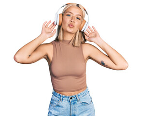 Beautiful young blonde woman listening to music using headphones looking at the camera blowing a kiss being lovely and sexy. love expression.