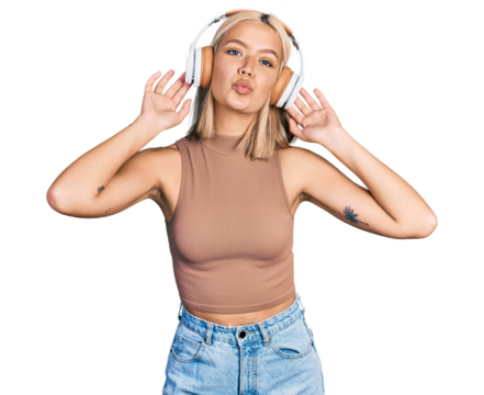 Beautiful young blonde woman listening to music using headphones looking at the camera blowing a kiss being lovely and sexy. love expression.