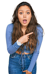 Young hispanic girl wearing casual clothes surprised pointing with finger to the side, open mouth amazed expression.