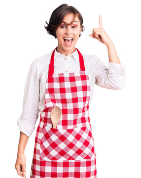 Beautiful young woman with short hair wearing professional cook apron pointing finger up with successful idea. exited and happy. number one.