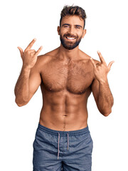 Young hispanic man wearing swimwear shirtless shouting with crazy expression doing rock symbol with hands up. music star. heavy concept.
