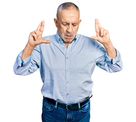 Senior man with grey hair and beard wearing casual blue shirt gesturing finger crossed smiling with hope and eyes closed. luck and superstitious concept.