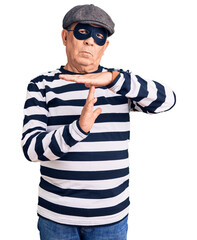 Senior handsome man wearing burglar mask and t-shirt doing time out gesture with hands, frustrated and serious face