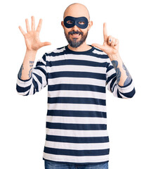 Naklejka premium Young handsome man wearing burglar mask showing and pointing up with fingers number seven while smiling confident and happy.