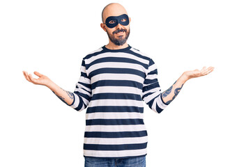 Naklejka premium Young handsome man wearing burglar mask smiling showing both hands open palms, presenting and advertising comparison and balance