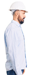 Young handsome man wearing architect hardhat looking to side, relax profile pose with natural face with confident smile.